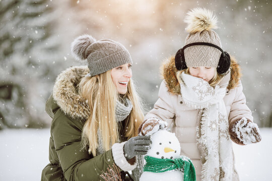 Mother and daughter build a snowman together in a beautiful winter landscape.