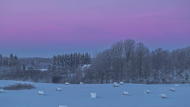 Night timelapse with the beginning of a new day in winter in a field with forgotten straw bales covered with snow - static shot - static shot