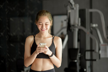 Fototapeta na wymiar Beautiful smiling woman using a phone while in a gym, Fitness and technology concept .