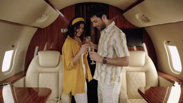 Smiling couple holding glasses of champagne in private jet.