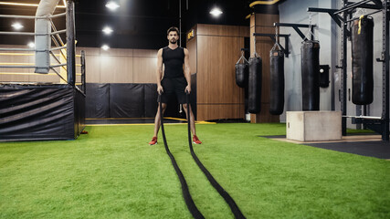 full length of bearded man working out with battle ropes.