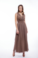 Fototapeta premium High fashion photo of beautiful elegant young woman in a pretty beige brown dress with a neckline, necklace posing on white background. Slim figure, make up, luxurious hair, shiny curls. Studio Shot