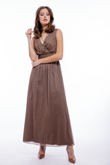 High fashion photo of beautiful elegant young woman in a pretty beige brown dress with a neckline, necklace posing on white background. Slim figure, make up,  luxurious hair, shiny curls. Studio Shot