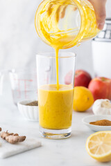 Pouring a detox smoothie into a tall glass from a the blender cup.