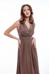 Naklejka premium High fashion photo of beautiful elegant young woman in a pretty beige brown dress with a neckline, necklace posing on white background. Slim figure, make up, luxurious hair, shiny curls. Studio Shot