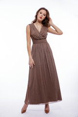 High fashion photo of beautiful elegant young woman in a pretty beige brown dress with a neckline, necklace posing on white background. Slim figure, make up,  luxurious hair, shiny curls. Studio Shot