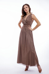 High fashion photo of beautiful elegant young woman in a pretty beige brown dress with a neckline, necklace posing on white background. Slim figure, make up,  luxurious hair, shiny curls. Studio Shot