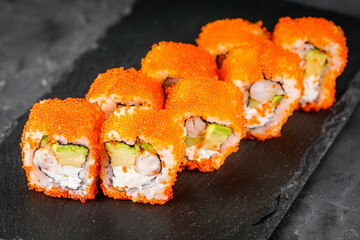appetizing sushi roll california with avocado shrimp cheese and masago caviar on a black stone plate