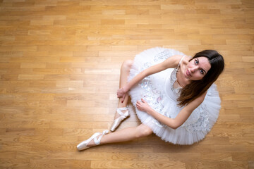 Ballerina in a white tutu on the floor looking up