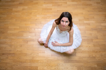 Ballerina in a white tutu on the floor looking up