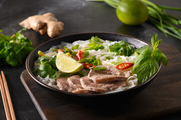 Pho Bo traditional Soup with beef, rice noodles, ginger, lime, chili pepper in bowl. Close up. Vietnamese and Asian cuisine.