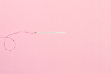 Aguja enhebrada con un hilo rosa en primer plano sobre un fondo rosa pastel liso y aislado. Vista superior y de cerca. Macro