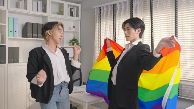 Asian businessman gay dancing in office workplace and hold LGBTQ flag.
