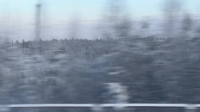 View of the winter forest landscape from the window of a moving train during a snowstorm with parallax effect