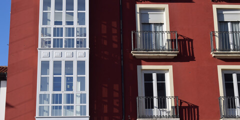 Fachada roja con ventanas y balcones blancas.