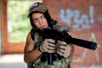 fit athlete woman with rifle gun aims at target, wearing military gear, in an abandoned building. focused confident brunette lady is ready to shoot at enemy, aiming weapon at target