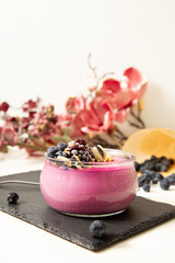 Fresh summer vegan tasty violet creamy dessert with organic blackberries and almonds in a jar on the stoneplate  with pink pastel flowers in the background. Food concept idea.