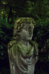 Stone garden statue of a female mythical head in a lush backyard.