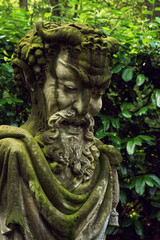 Stone garden statue of a male mythical head in a lush backyard.