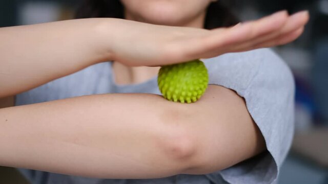 Woman doing exercises with rubber ball on white background, closeup. young woman massages her elbow with spiky trigger point ball, tennis elbow exercises