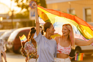 Young lesbian couple walking with rainbow flag during pride parade