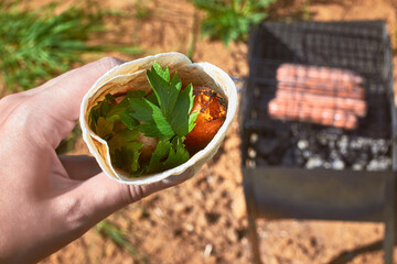 Barbecue sausages on the grill on the grill, wrapped in pita bread with parsley and sauce. A typical country picnic.