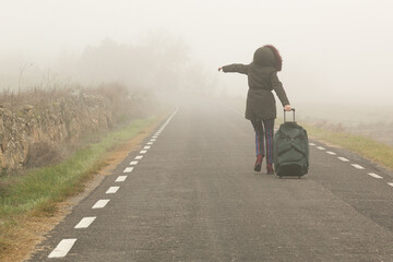 Con una bolsa maleta una mujer camina por la carretera con mucha niebla, parte trasera