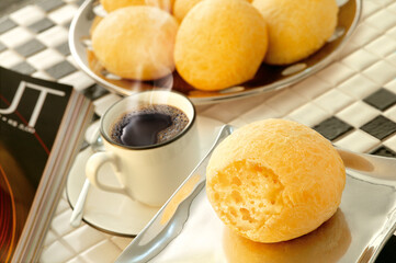 mesa de café da manhã com pão de queijo e xícara com café preto saindo fumaça