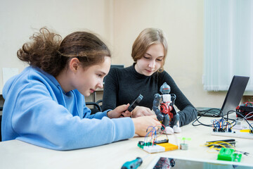 Two teenager girl at robotics school makes robot managed from the constructor, children learn robot constructing.