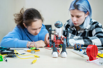 Two teenager girl at robotics school makes robot managed from the constructor, children learn robot constructing at STEM engineering science education class.