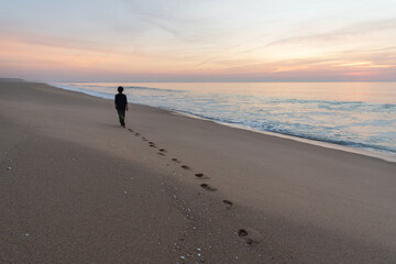 Naklejka premium Woman walking at dusk on a beach in Alentejo leaves her footprints on the sand