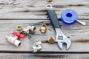 Various plumbing spare parts, sealing tape and adjustable wrench on rustic wooden background