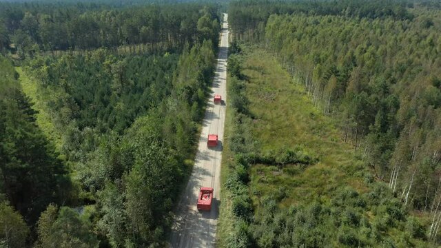 Aerial: red firefighters trucks driving along a forest road. Heavy all terrain vehicles and firetrucks on dirt road. Drone following convoy of fire fighting machines. Firemen inspecting wildfires