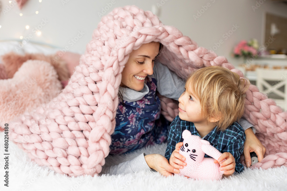 Sticker Beautiful blond boy and mother, lying in bed, hiding under blanket, enjoying family time