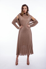 Fototapeta premium High fashion photo of a beautiful elegant young woman in a pretty long beige brown dress, cardigan posing on white background. Studio shot. Slim figure, make up, luxury hair, shiny curls