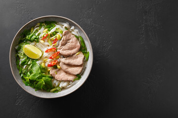 Pho Bo Soup with beef, rice noodles, lime, chili pepper in gray bowl isolated on black background. Popular Vietnamese and Pan-Asian cuisine.