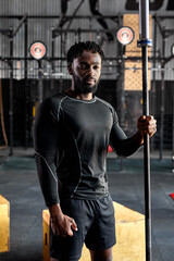 Young afro american athlete male in black sportswear holding barbell bar, preparing for cross fit training, young handsome guy posing at camera, looking confident and strong. Muscular sportsman