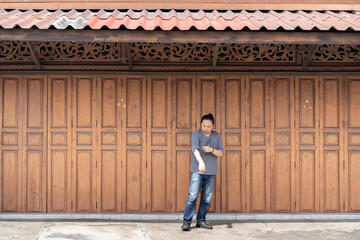 Asian long hair man is standing and posting in front of Classic backdrop wood wall and door in front of Thailand vintage traditional Building.