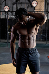 Fototapeta na wymiar Fit strong muscular african american male with naked torso posing at camera, in gym indoors,handsome young black guy having rest after training, workout. man touching head, looking down