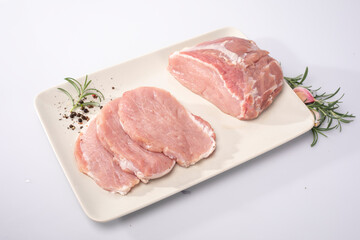 Raw pork meat, loin, ham in chops and in cross-section on a white plate, on white background, top view. Packshot photo.