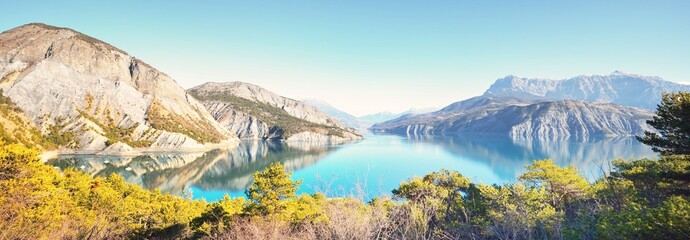 Panoramic view of the mountain lake Lac de serre-poncon in French Alps on a sunny day. Clear blue sky, still water. Travel destinations, tourism, landmark, nature, Christmas vacations in France - obrazy, fototapety, plakaty