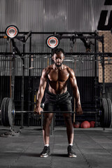 Naklejka na ściany i meble Young muscular african sweaty fit man with big muscles training with heavy barbell weight during cross training workout in modern gym. handsome guy is engaged in sport, fitness, pumping arm muscles