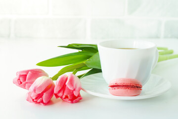 three pink tulips, macarons and a cup of coffee on a white table..