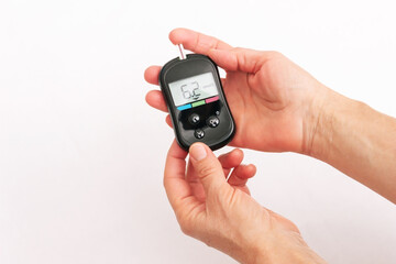 Close-up of the hands of a an elderly woman using a glucose meter to measure blood sugar isolated on a white background. Checking blood sugar level by glucometer for diabetes testing. Health care