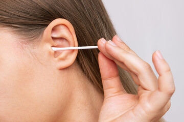Obraz premium Cropped shot of a young caucasian woman cleaning her ear with a cotton swab isolated on a white background. Hygiene and health care concept
