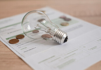 Electricity bill with light bulb and several coins. Concept of electricity prices and tax payments.