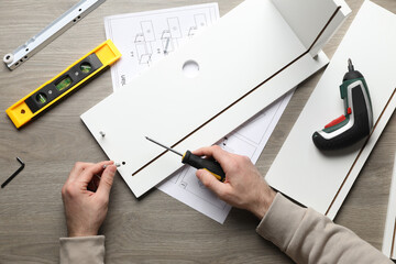 Man with screwdriver assembling white furniture at table, top view