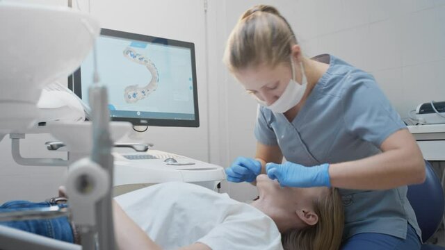 Doctor woman makes a 3d scan of the teeth of a female patient. Creates a 3D model of the jaw, heals the mouth. Dental clinic. Uses a smart device oral cavity scanner on the monitor.