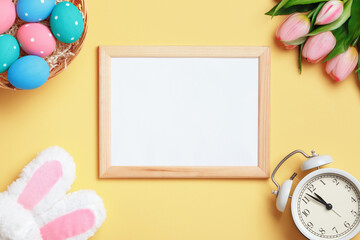 Easter composition. Frame eggs tulips alarm clock on a yellow background. Flat lay invitation card with copy space.