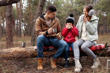 Happy family with sandwiches and hot drinks in forest